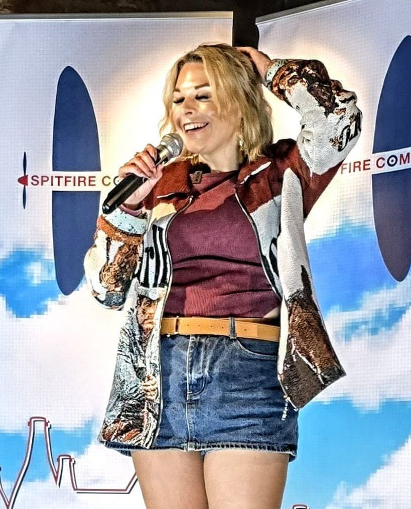 A comedian laughing on stage in front of the Spitfire Comedy banner