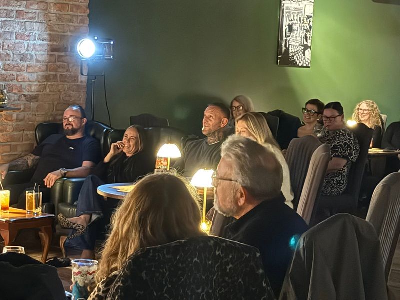 The audience laughing at a Spitfire Comedy night, lit by table lamps and a stage light