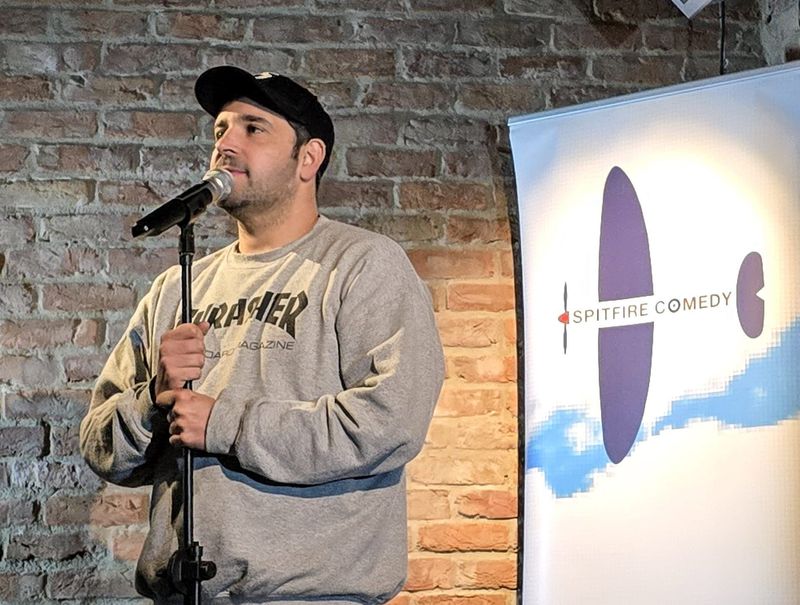 A comedian at the mic stand beside the Spitfire Comedy banner